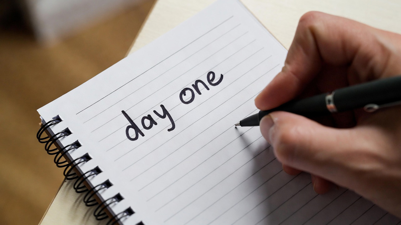 Notepad with someone writing ‘day one’ across the top of the page